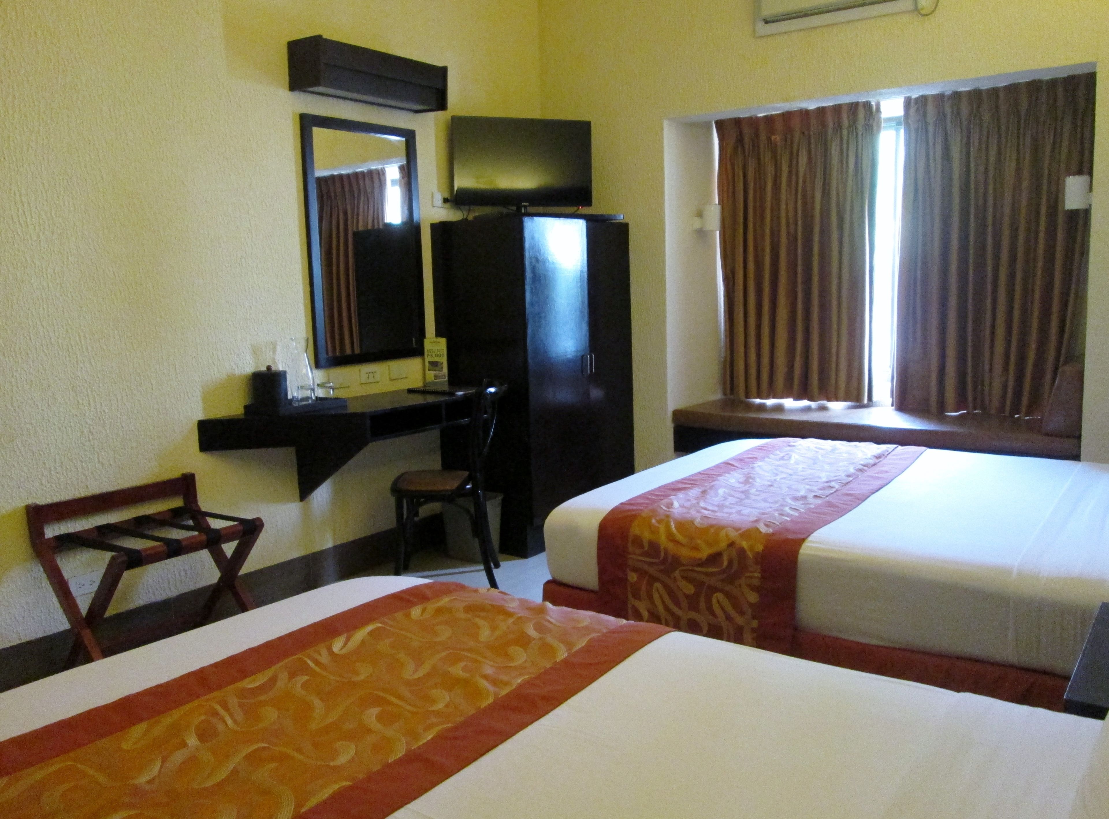 A hotel room with two beds, a desk with a chair, a television, and a window with curtains.