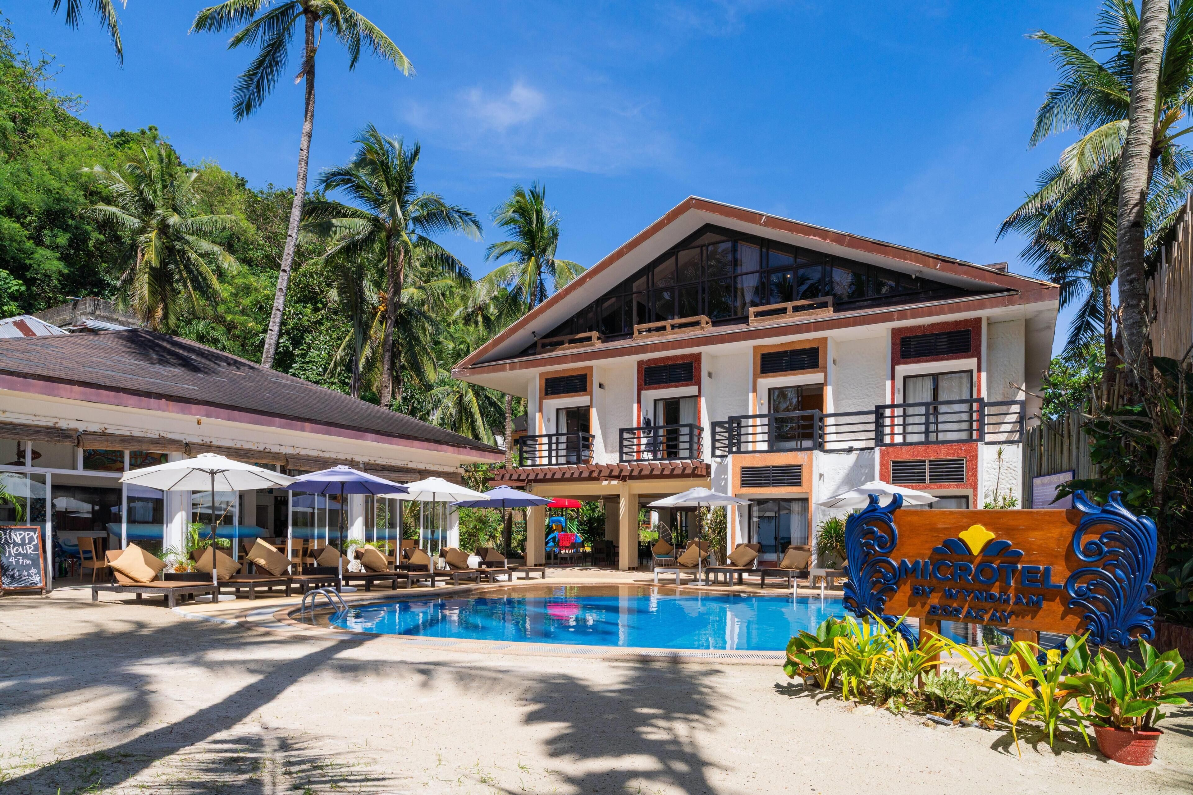 A hotel with a swimming pool, lounge chairs, and palm trees.