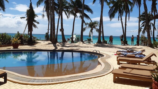 A pool area with lounge chairs, palm trees, and a view of the ocean.