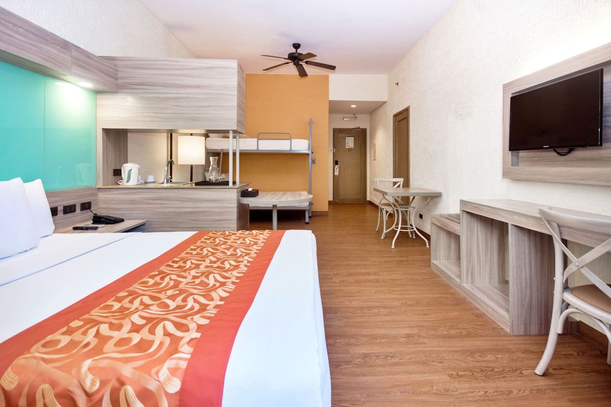 Habitación de hotel con una cama grande, un escritorio, una silla, un televisor y un ventilador de techo.
