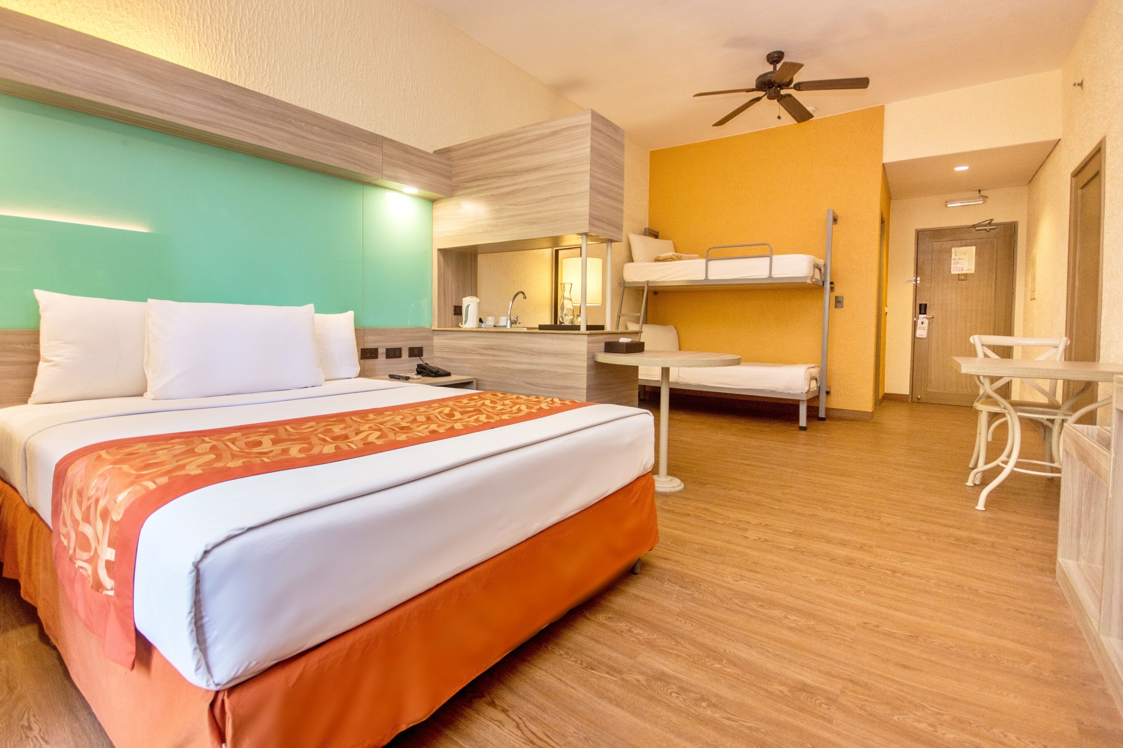 A hotel room with a large bed, a bunk bed, a desk, and a chair.