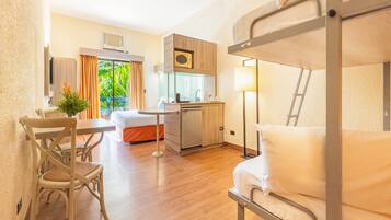 Quarto de hotel compacto com beliche, escrivaninha com cadeira, pequeno espaço de cozinha e janela com cortinas.