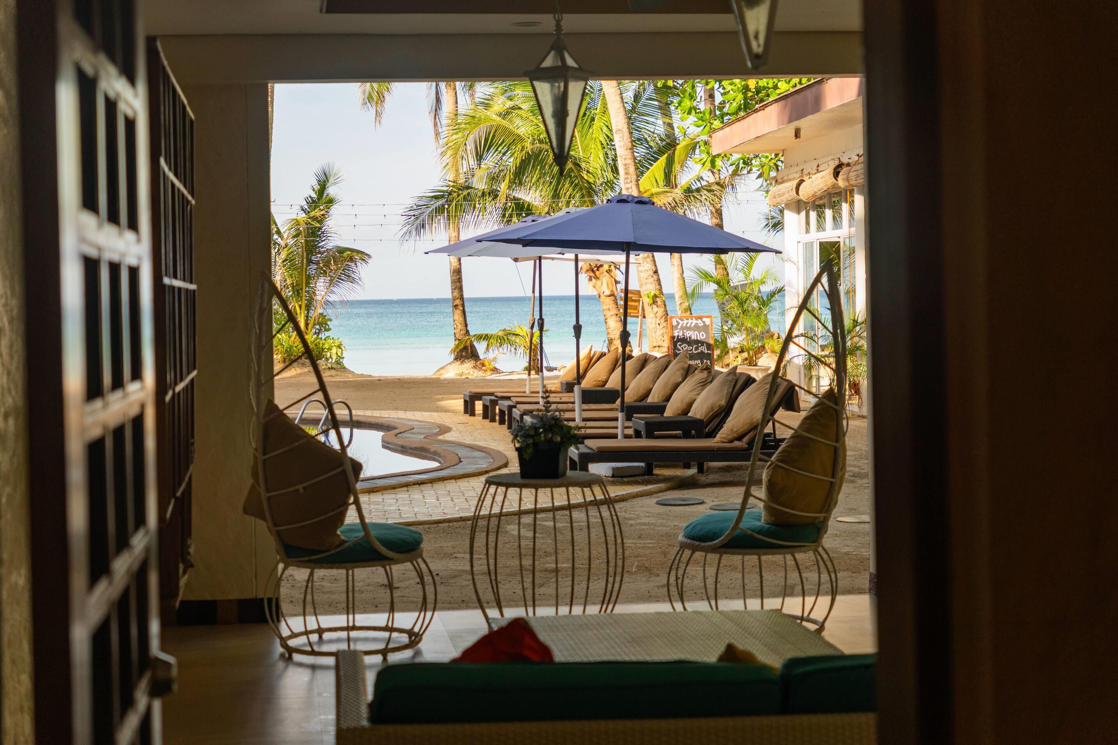 A beachside lounge with a view of the ocean, outdoor seating, and a sign indicating a Filipino special.