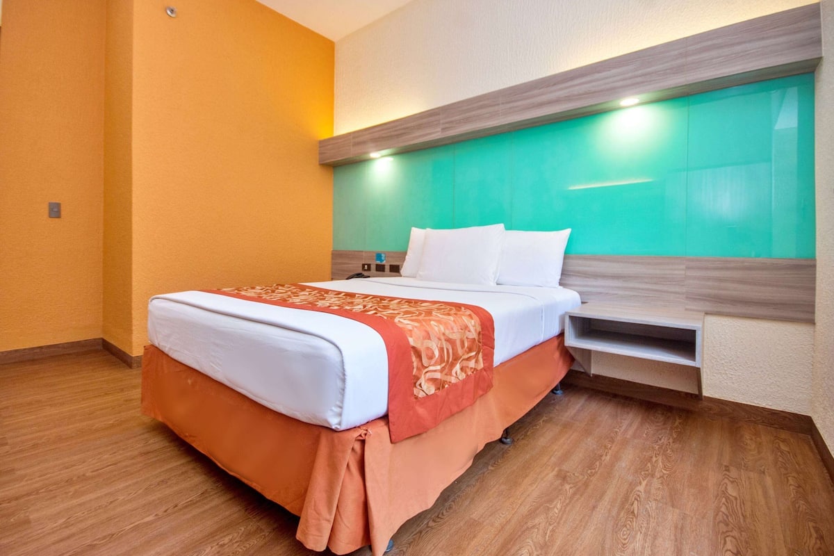 Una habitación de hotel con una cama, una mesita de noche y un estante fijado a la pared.