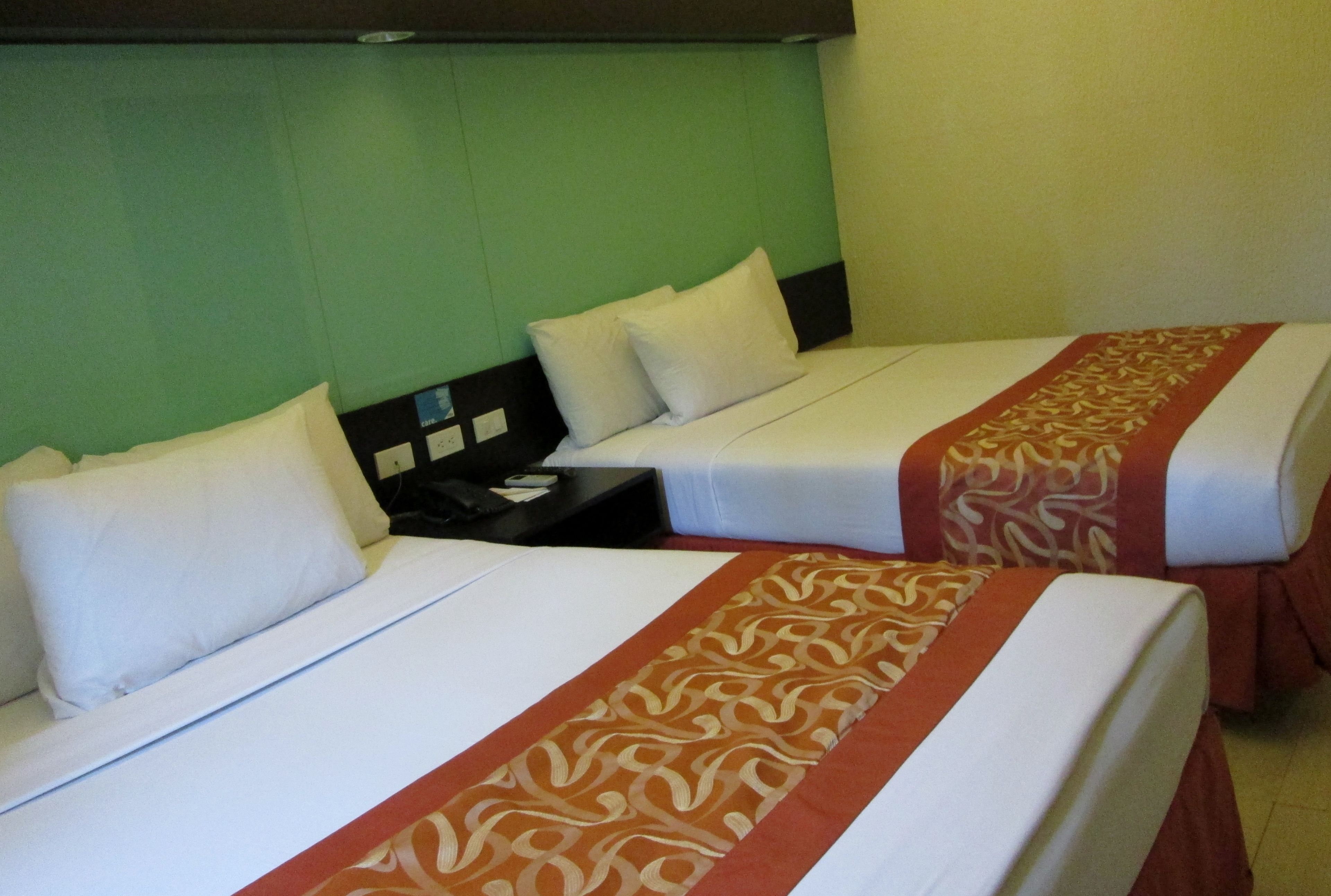 Two single beds with white linens and a patterned runner, a nightstand, and a green wall.