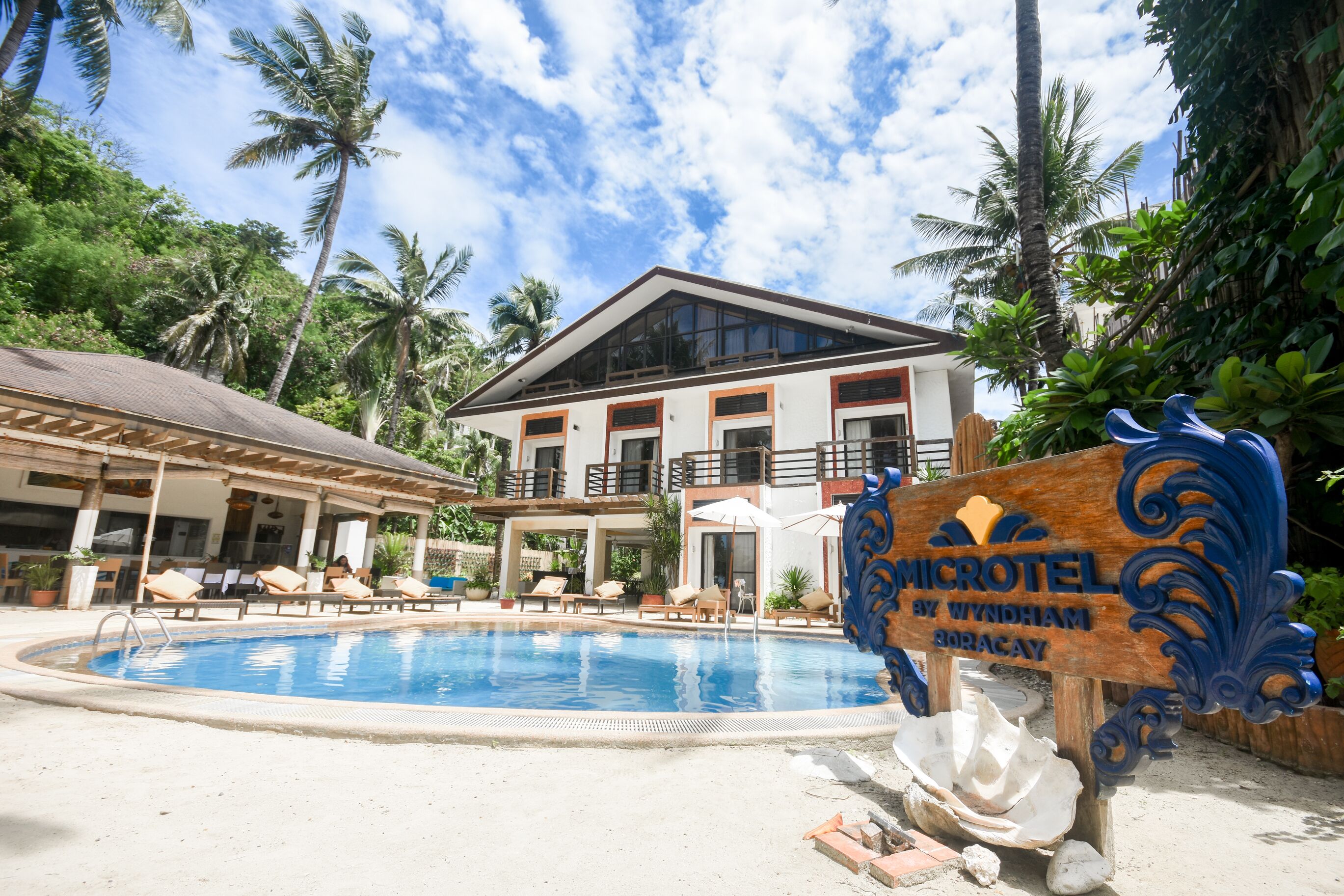 Zona de piscina con sillones de descanso y un cartel que dice 'MICROTEL BY WYNDHAM BORACAY'.