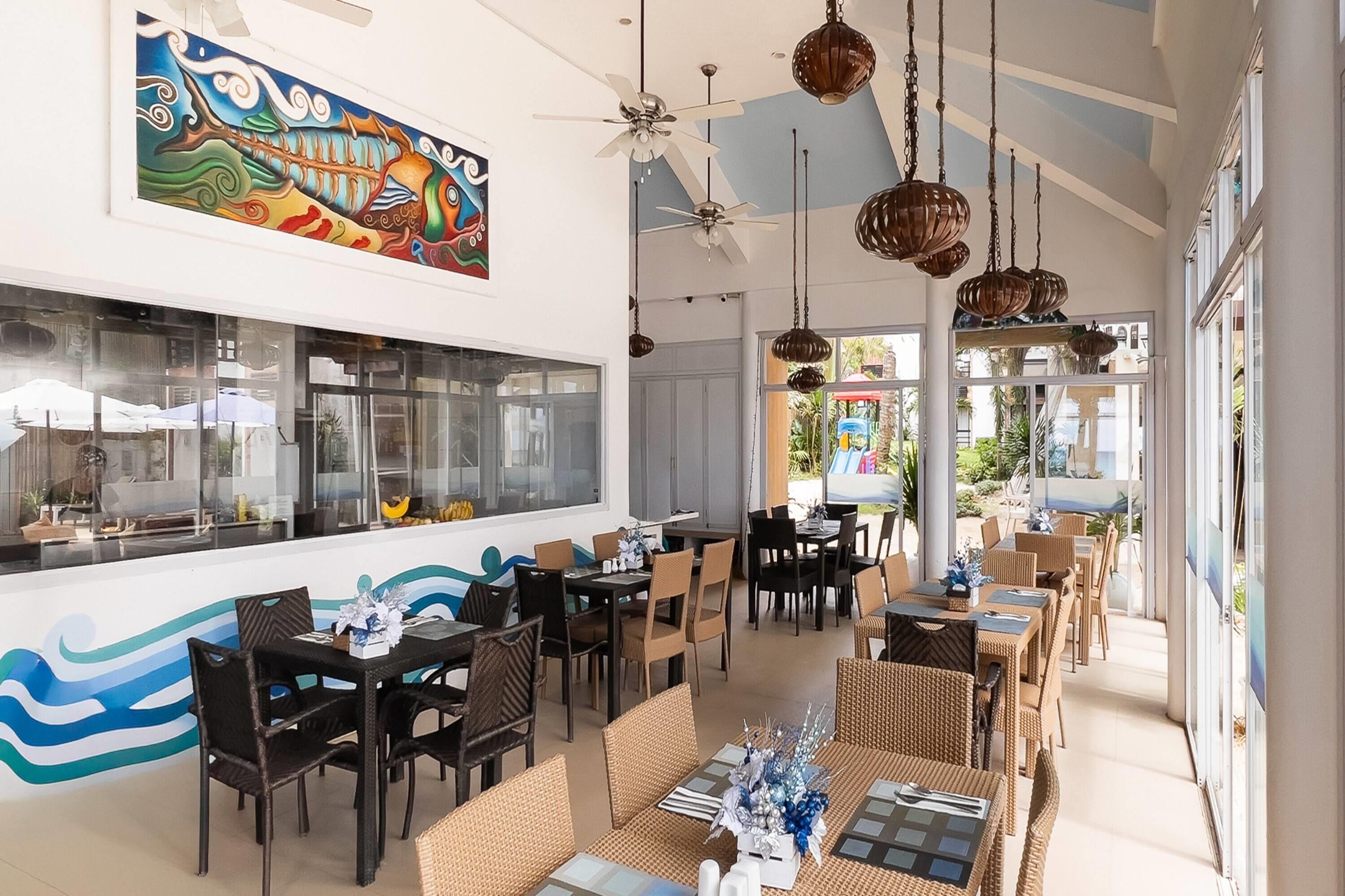 A restaurant with a modern interior, featuring a long counter, multiple dining tables, and hanging pendant lights.