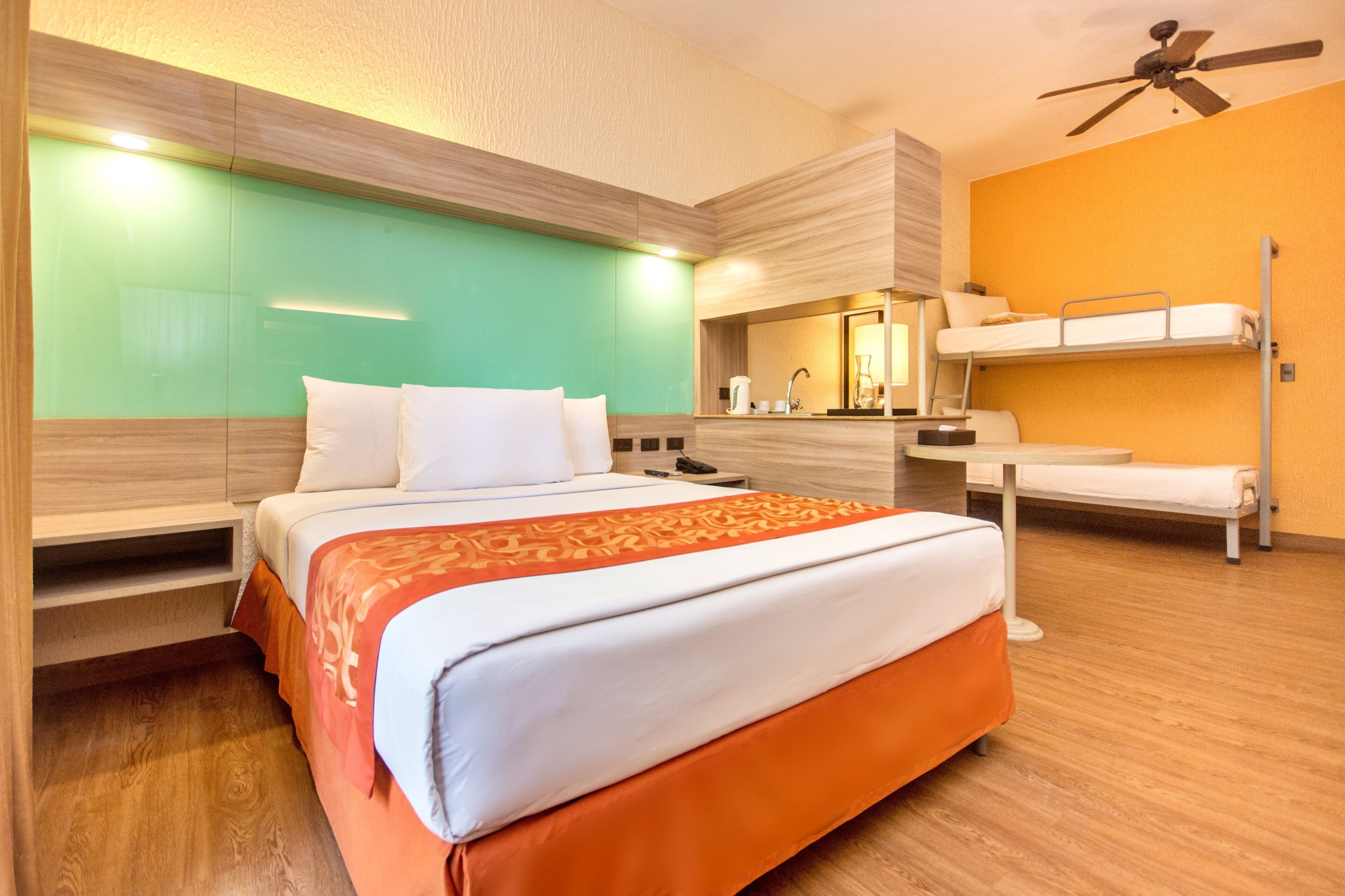 A hotel room with a bed, a bunk bed, a ceiling fan, and a bathroom with a mirror and sink.