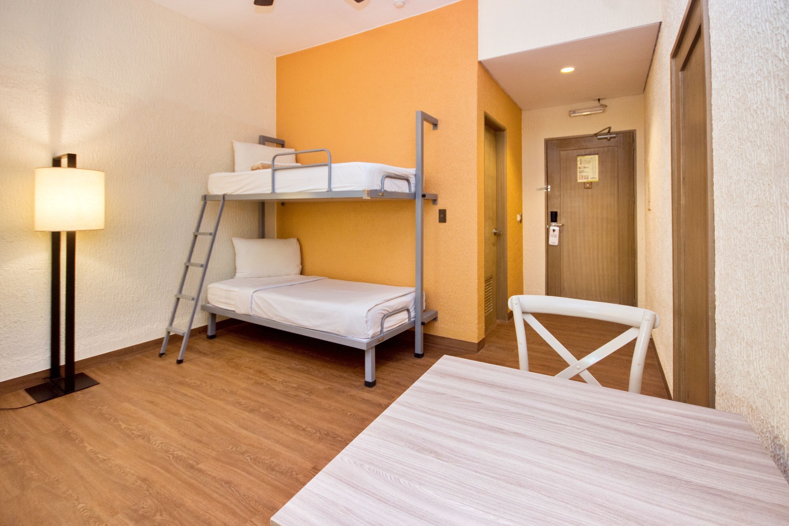 A compact room with bunk beds, a desk, a chair, and a lamp.