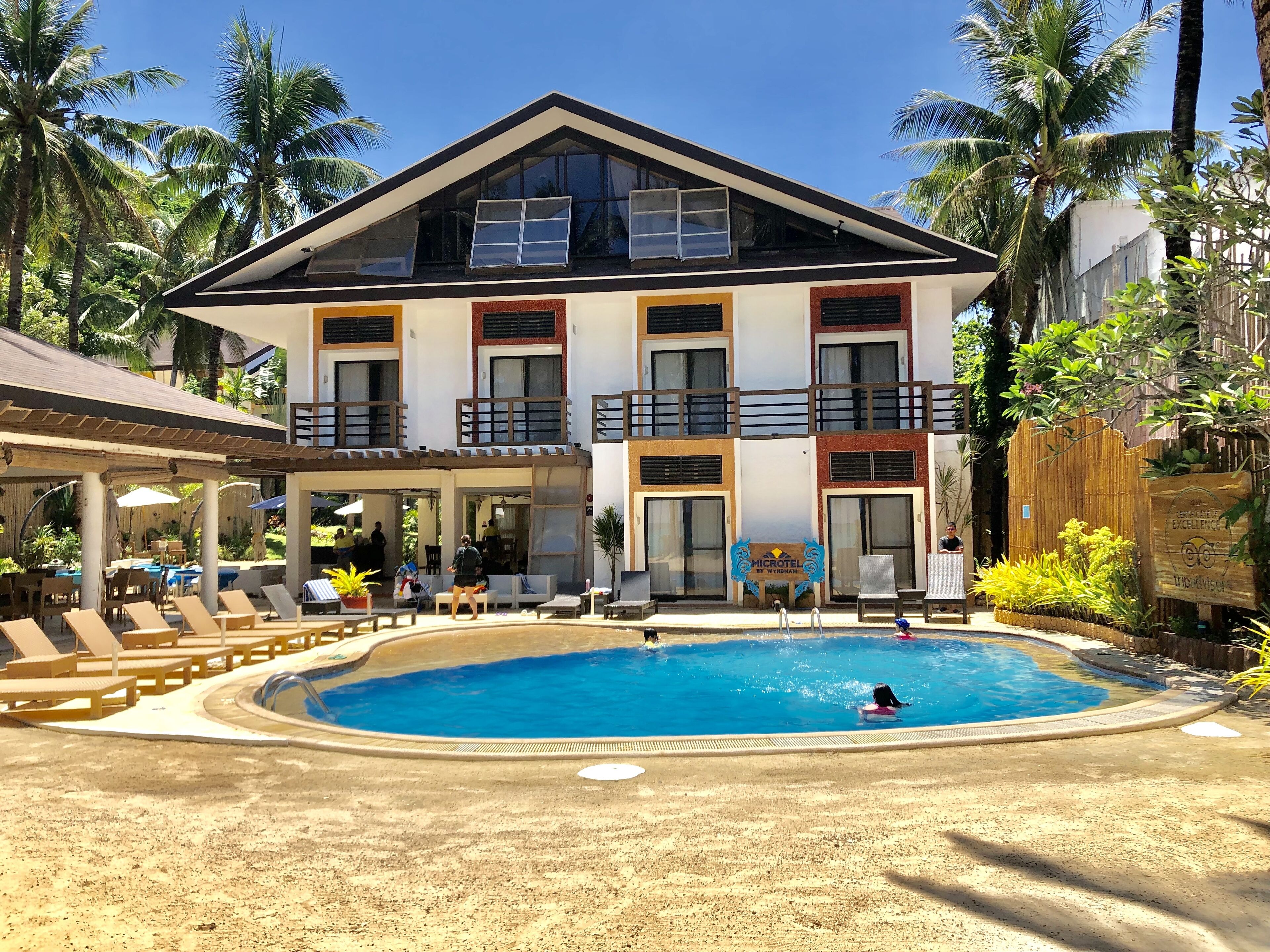 Un edificio de dos pisos con piscina, asientos exteriores y palmeras.