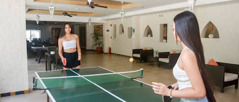 A spacious indoor area with a ping pong table, seating arrangements, and ceiling fans.