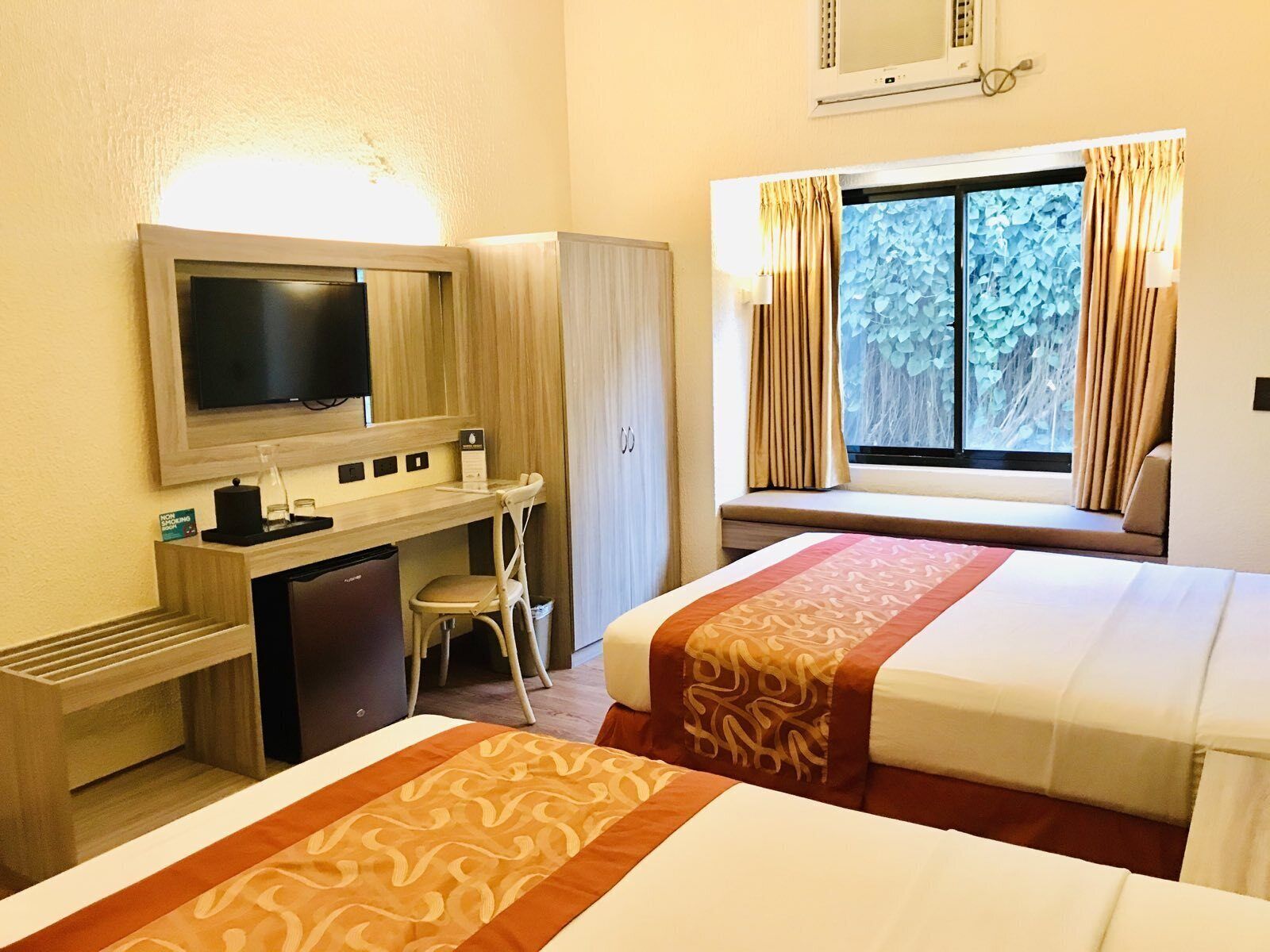 Habitación de hotel con dos camas, un escritorio, una silla, un televisor y una ventana con cortinas.