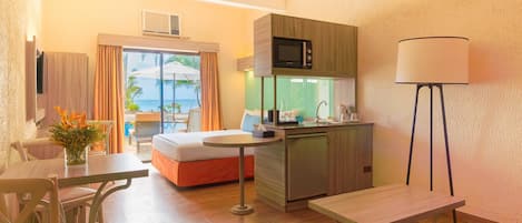 Habitación de hotel compacta con cama, pequeña kitchenette, mesa de comedor y vista al océano.