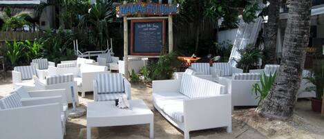 Un espace extérieur aménagé dans un style tropical, avec des meubles en osier blanc et une enseigne indiquant « Mama’s Fish House ».