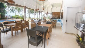A restaurant with outdoor seating overlooking a pool, featuring wicker furniture and hanging light fixtures.
