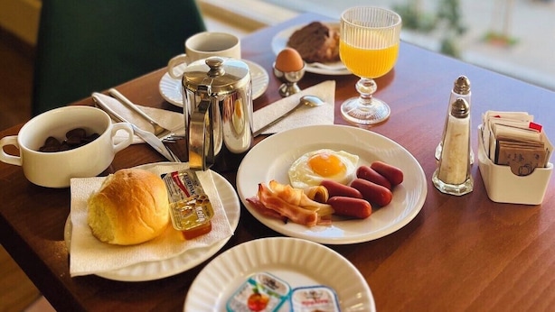 Una mesa de desayuno con un croissant, huevos, salchichas y un vaso de jugo de naranja.