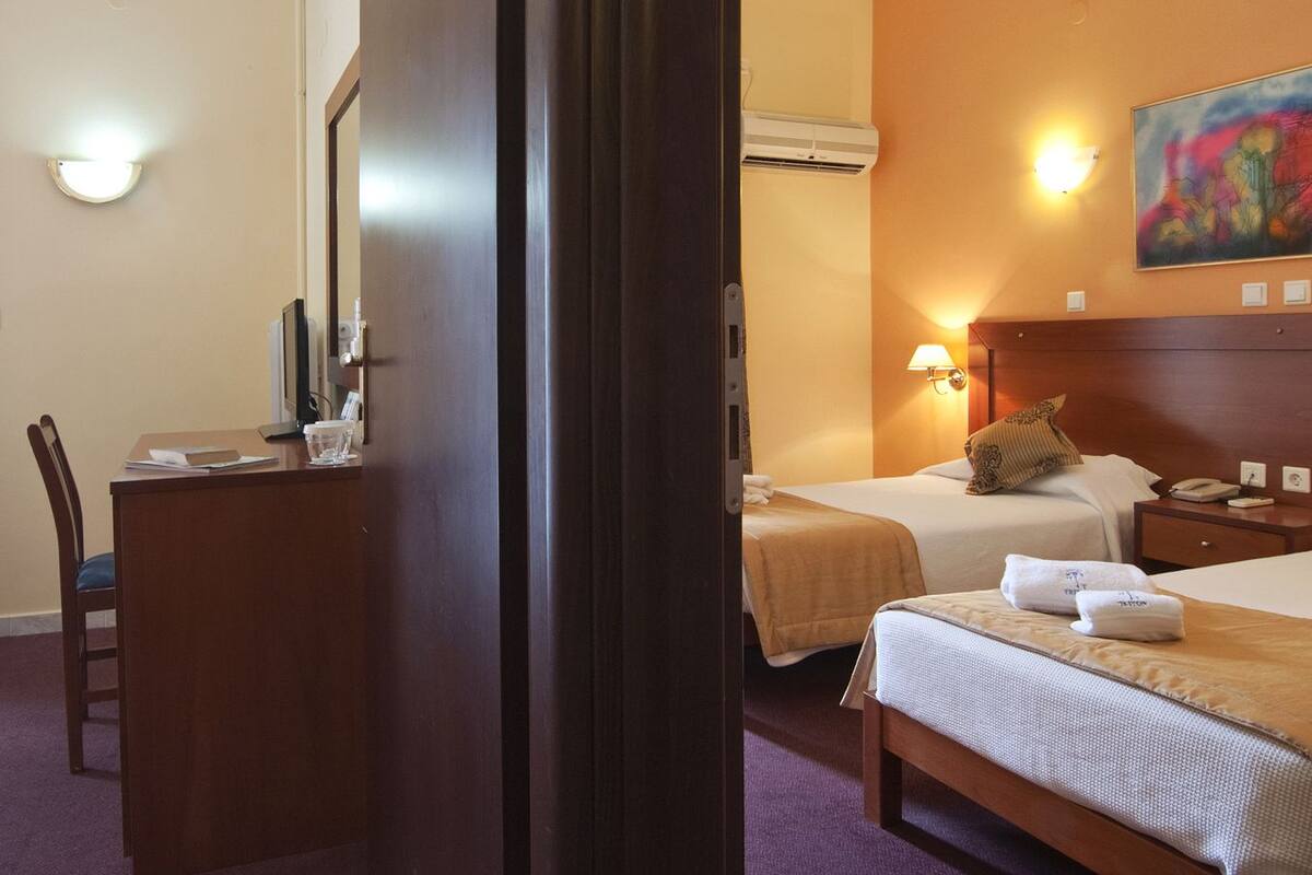 Habitación de hotel con dos camas, un escritorio, una silla, un equipo de aire acondicionado y un cuadro en la pared.