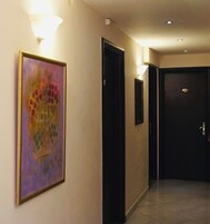 Un pasillo con un cuadro abstracto enmarcado, una puerta negra y una lámpara fijada a la pared.