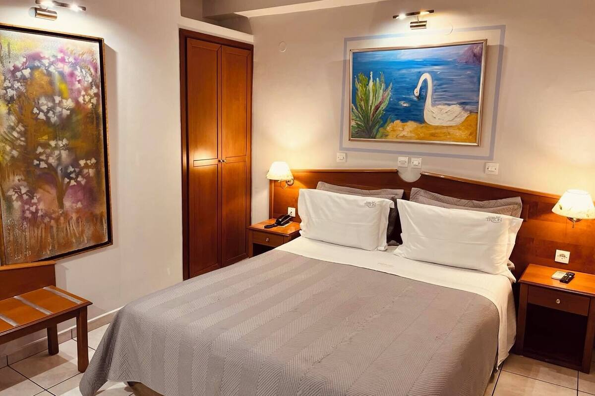Habitación de hotel con una cama, mesitas de noche, un armario de madera y dos cuadros en las paredes.