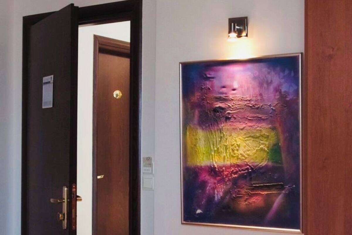Un pasillo con una puerta de madera, un banco con un libro y un cuadro abstracto y colorido.