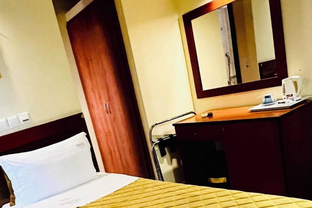 Habitación de hotel con una cama, cabecera de madera, mesita de noche, espejo y un pequeño escritorio con una silla.