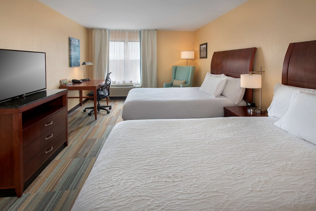A hotel room with two beds, a desk with a TV, a chair, and a lamp.