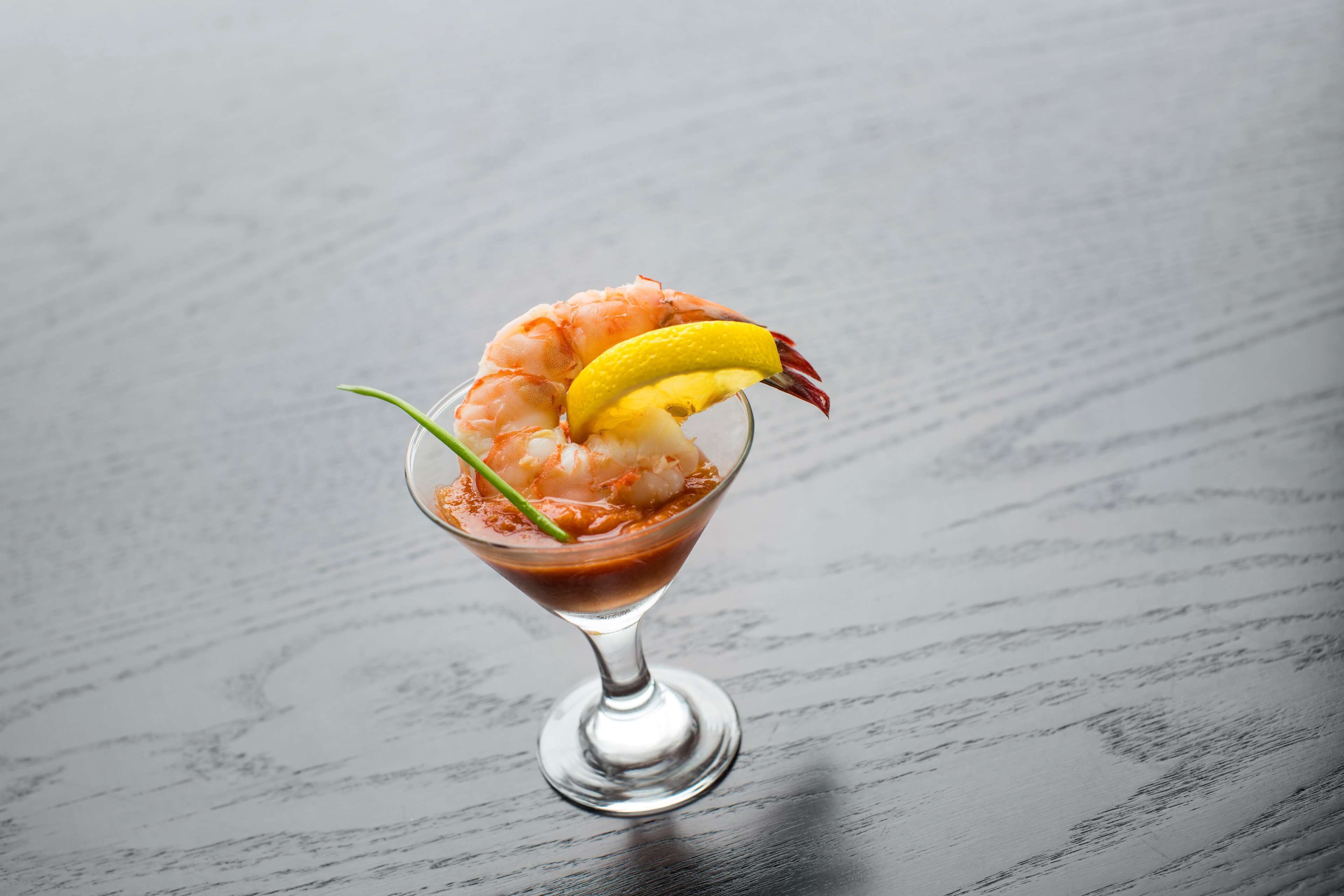 A cocktail in a martini glass with shrimp and lemon garnish.