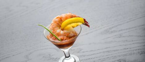 A cocktail in a martini glass with shrimp and lemon garnish.