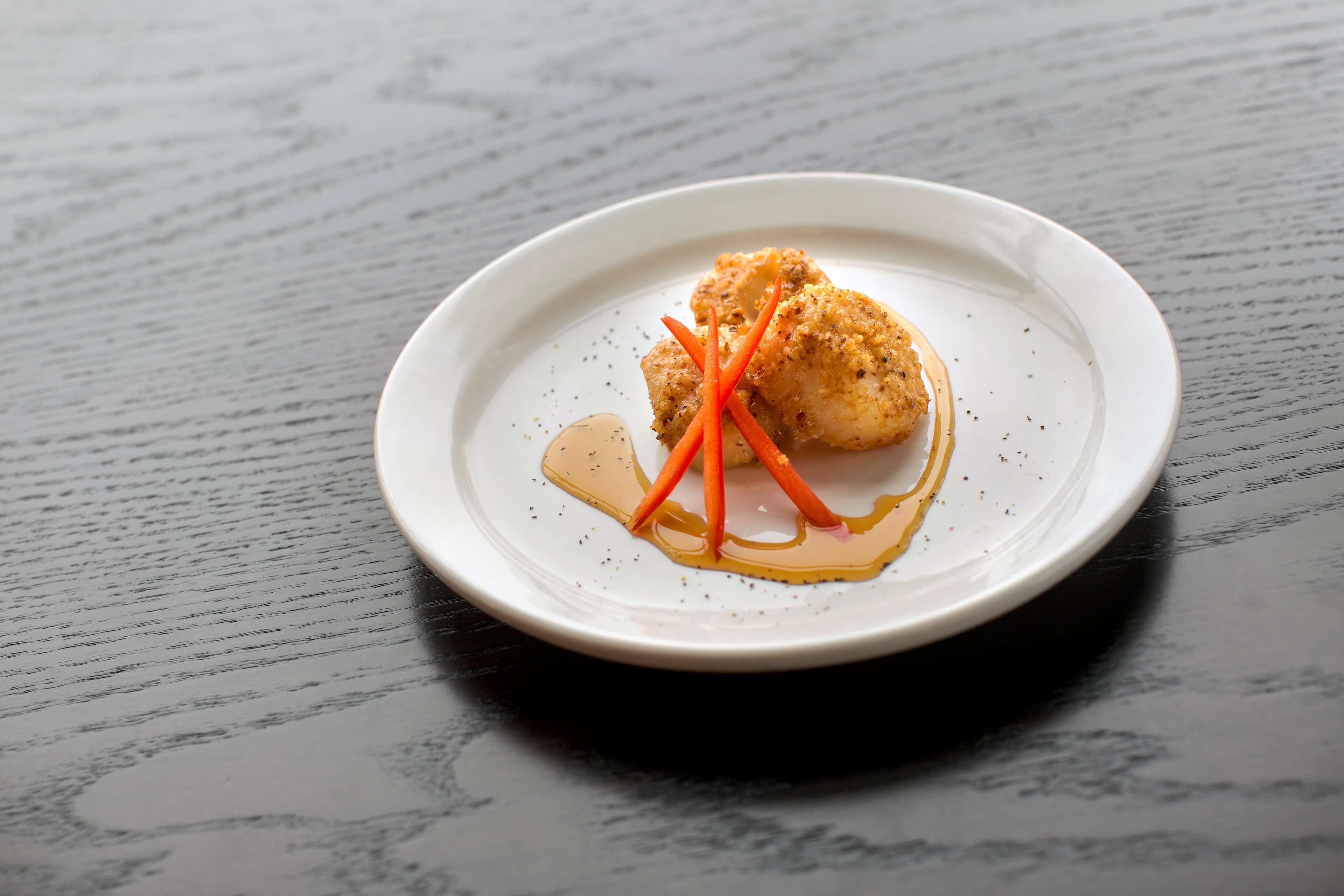 A white plate with a piece of food, possibly a fish fillet, on a dark wooden table.