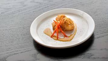 A white plate with a piece of food, possibly a fish fillet, on a dark wooden table.
