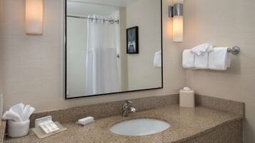 A bathroom with a granite countertop, a white sink, a mirror, a towel rack with towels, a framed picture, and a tissue dispenser.