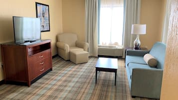 Ein Hotelzimmer mit Fernseher, einem beigen Sessel, einem blauen Sofa, einem Holzkleiderschrank und einem karierten Teppich.