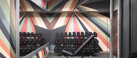 Un gimnasio con un diseño de pared colorido, una banca y filas de mancuernas.