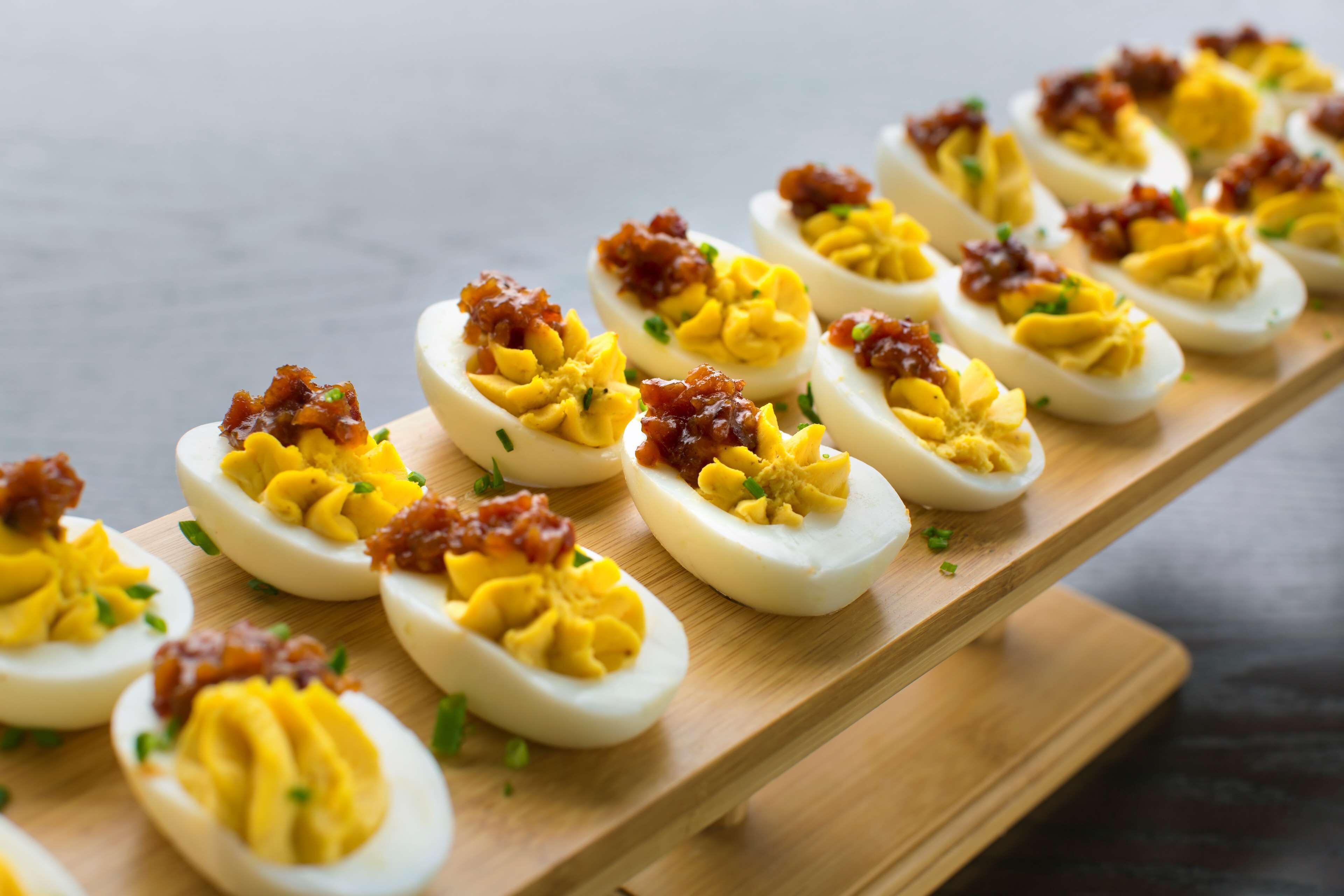 Una tabla de madera con huevos rellenos adornados con tocino y hierbas.