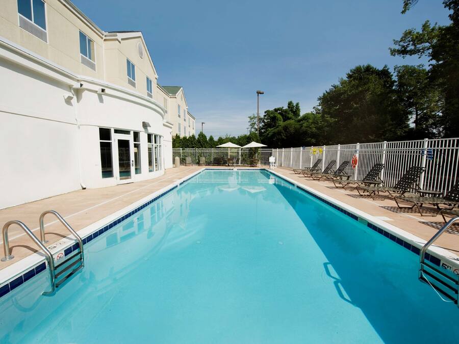 A swimming pool with metal railings, a tiled deck, and a white building with windows.