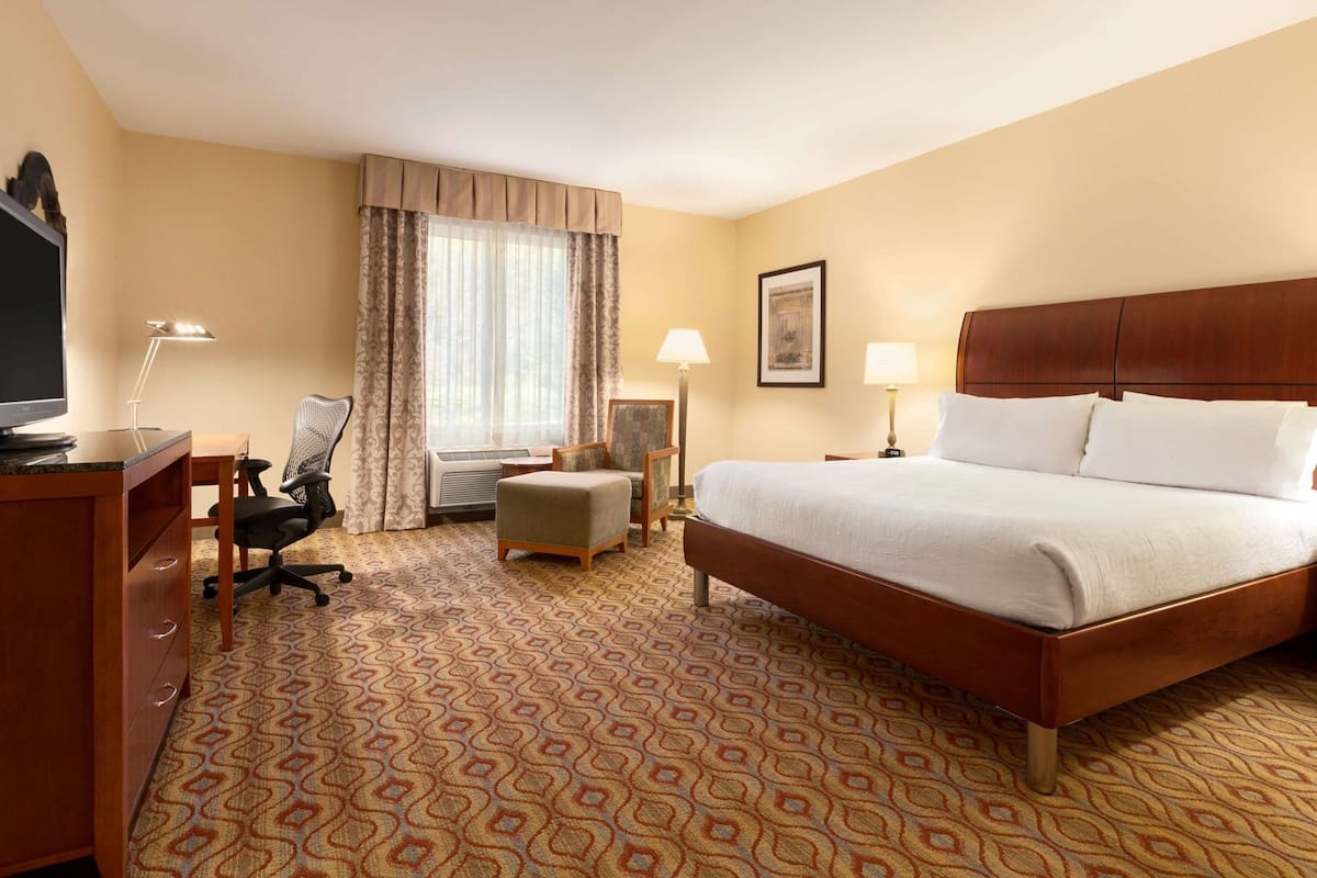A hotel room with a bed, desk, chair, and a television.