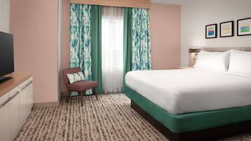 A hotel room with a large bed, a desk with a television, a chair, and a window with curtains.