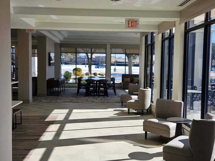 A spacious lobby with a high ceiling, large windows, and a central seating area with chairs and tables.