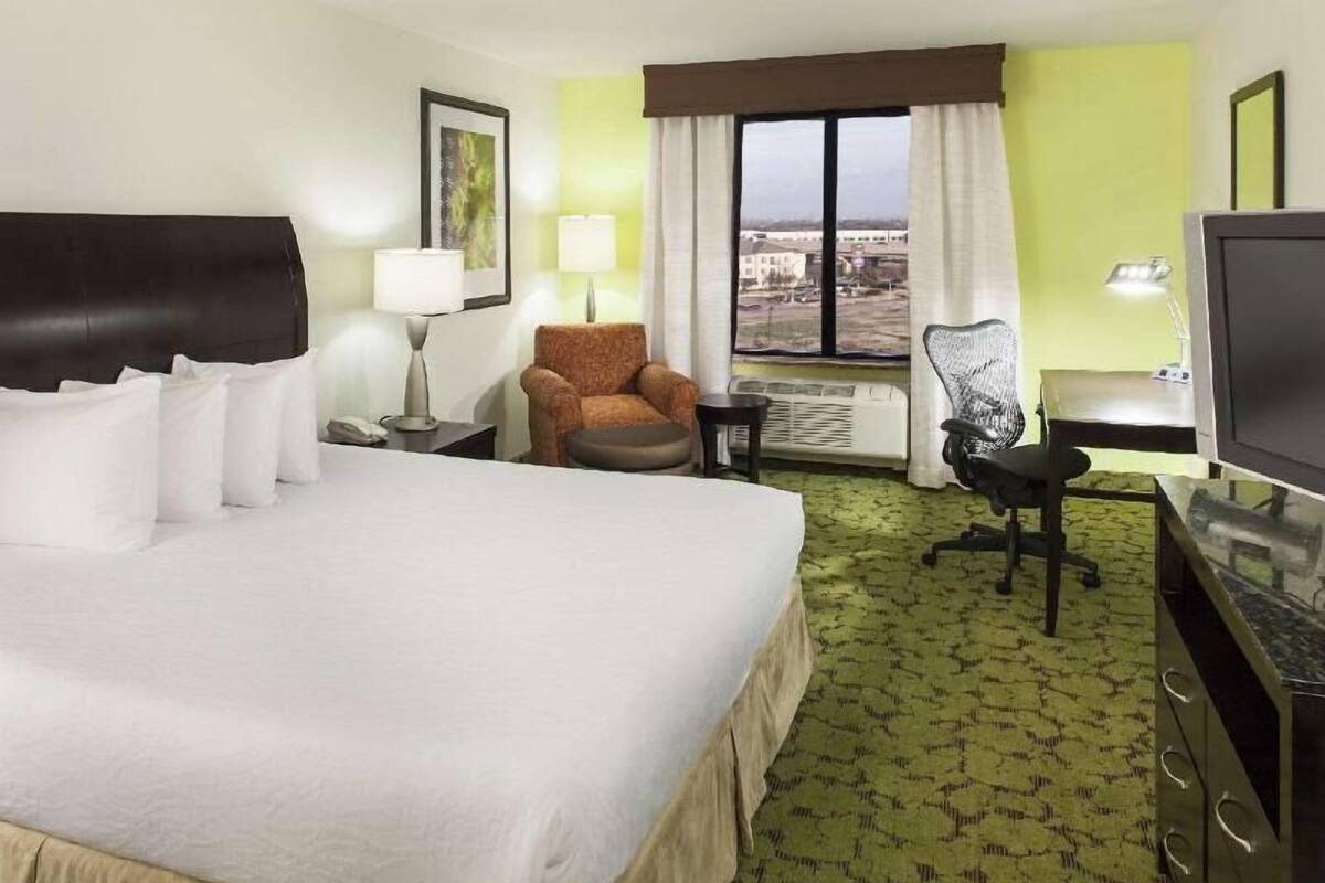 A hotel room with a bed, a chair, a desk, a television, and a window with a view.