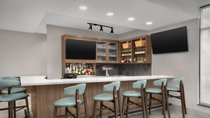 A bar area with a white countertop, wooden cabinets, and bar stools. - Hilton Garden Inn Dallas Lewisville (Lewisville)