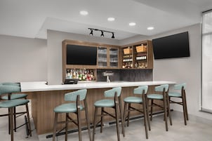 A bar area with a white countertop, wooden cabinets, and bar stools.