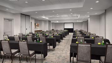 Un salón de conferencias con filas de mesas y sillas, equipado con proyectores y pantallas.