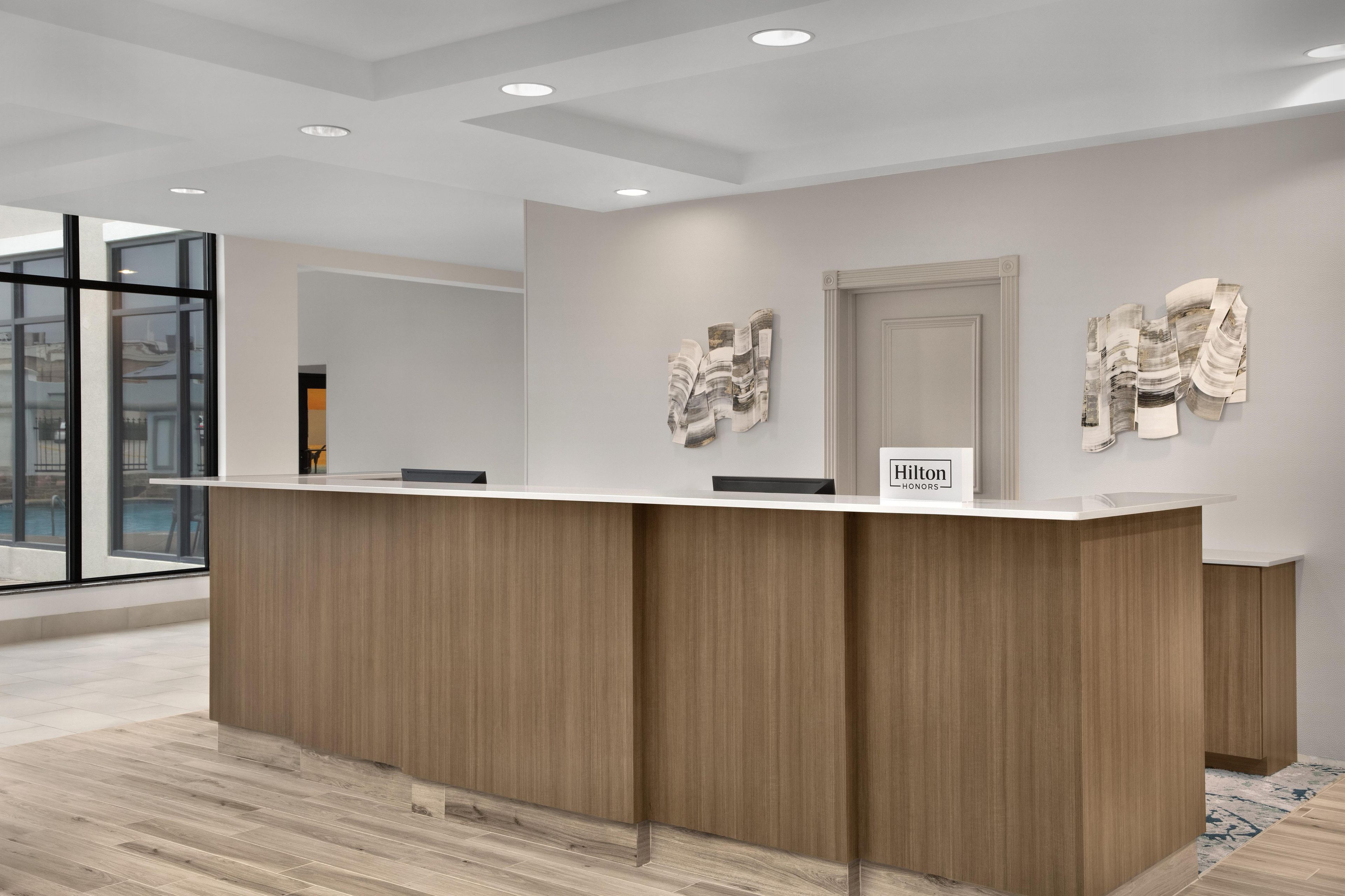 A reception desk with a wooden finish, a glass partition, and two abstract wall art pieces.