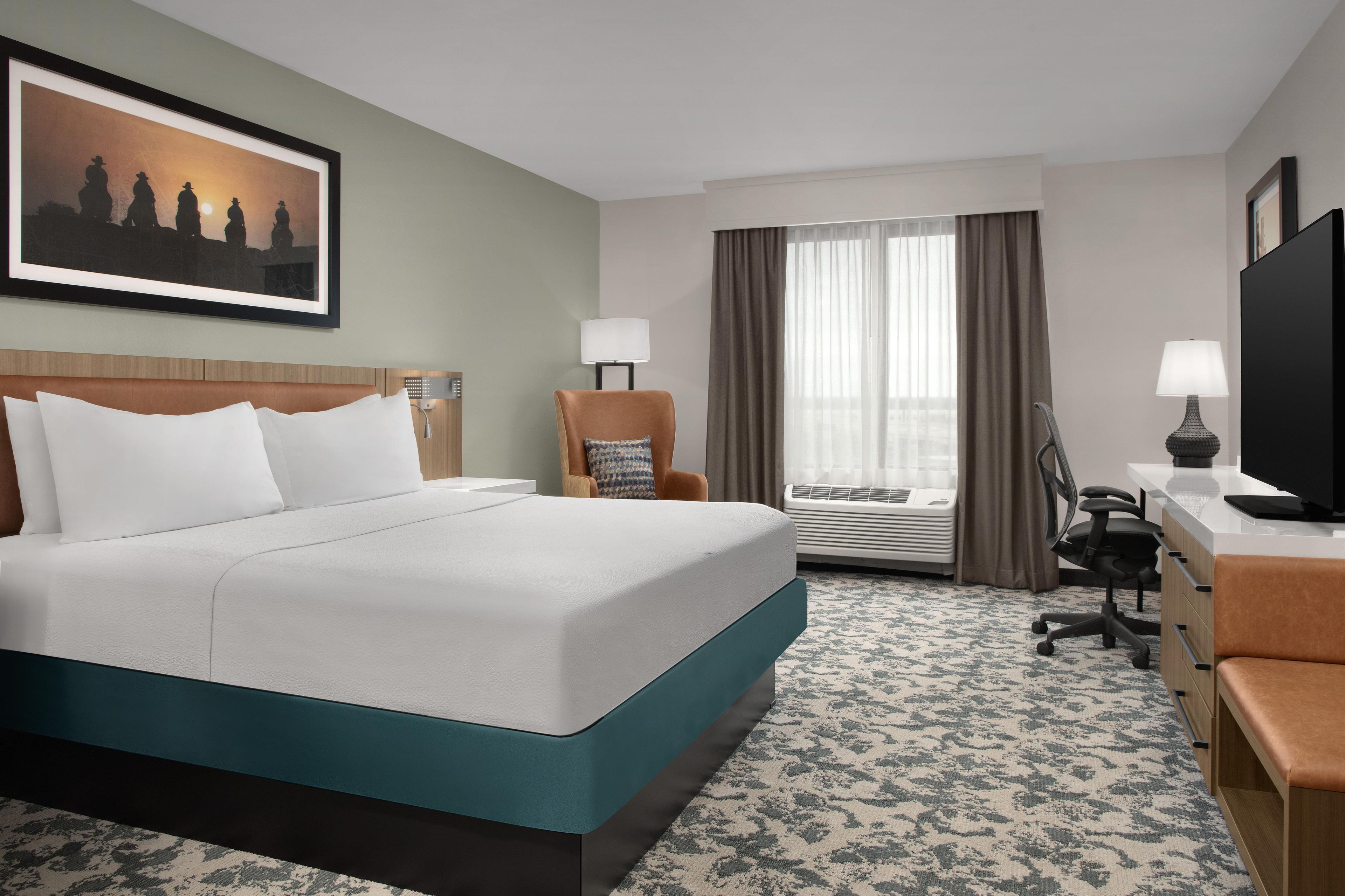 A hotel room with a large bed, a desk, a chair, a television, and a window with curtains.