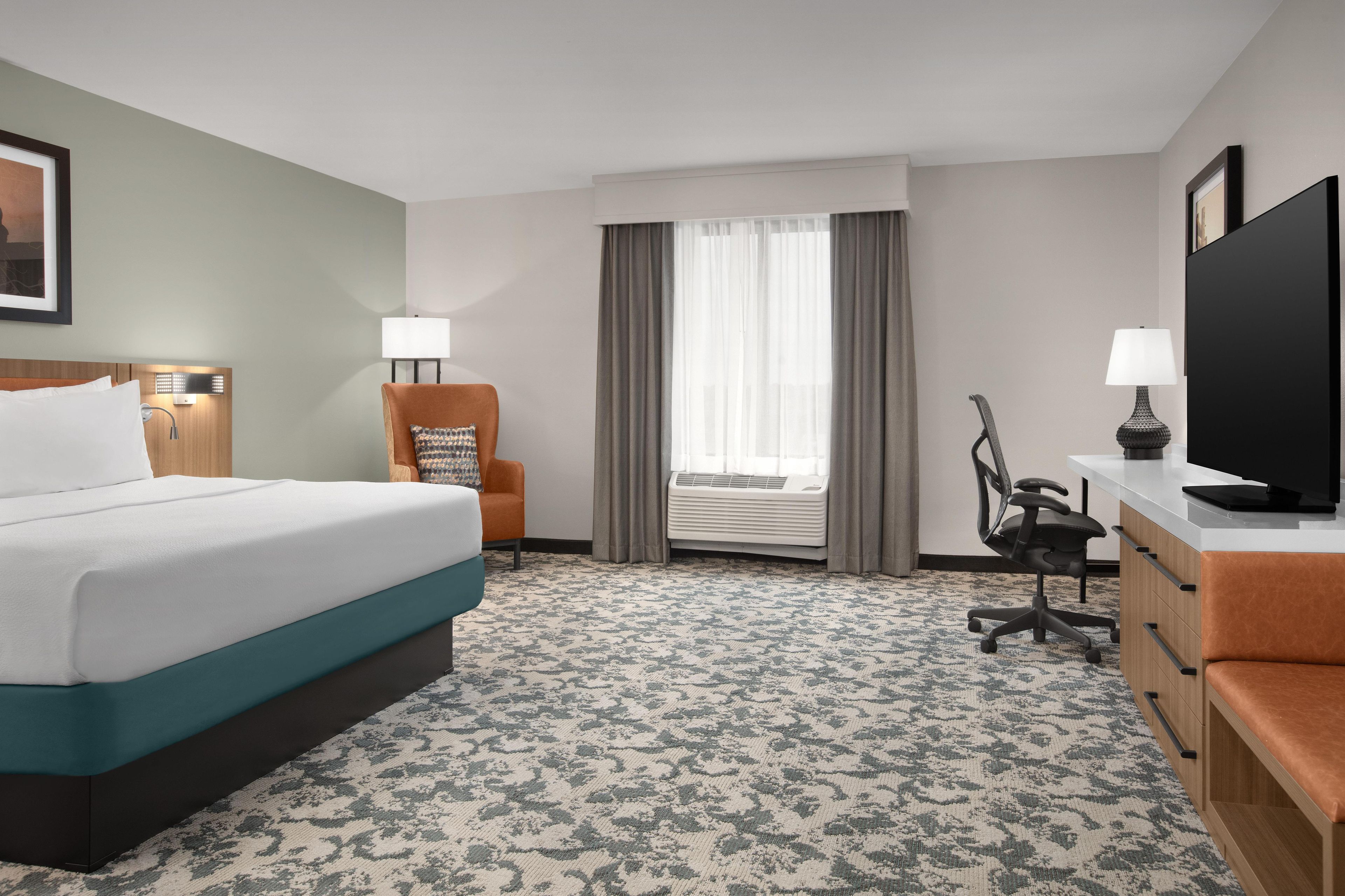 A hotel room with a bed, a desk, a chair, a television, and a window with curtains.