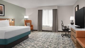 A hotel room with a bed, a desk, a chair, a television, and a window with curtains.