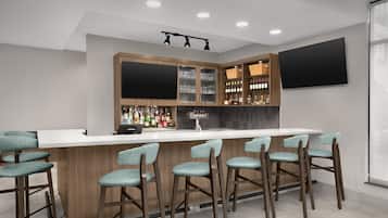 A bar area with a white countertop, wooden cabinets, and bar stools.