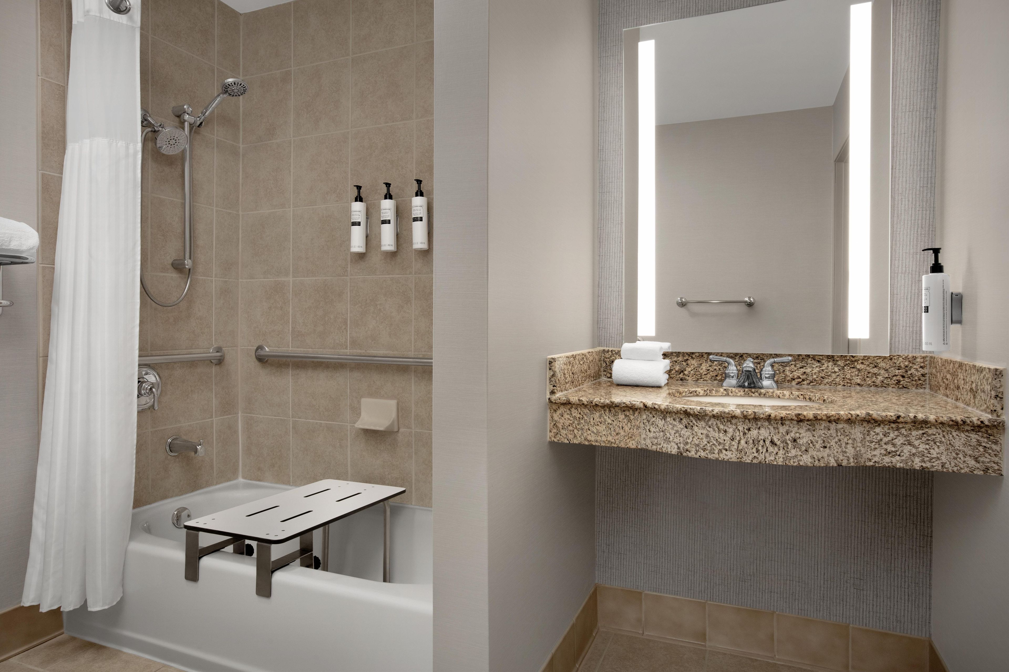 Een moderne badkamer met een douche, handgrepen, een wastafel met een granieten blad en een spiegel.
