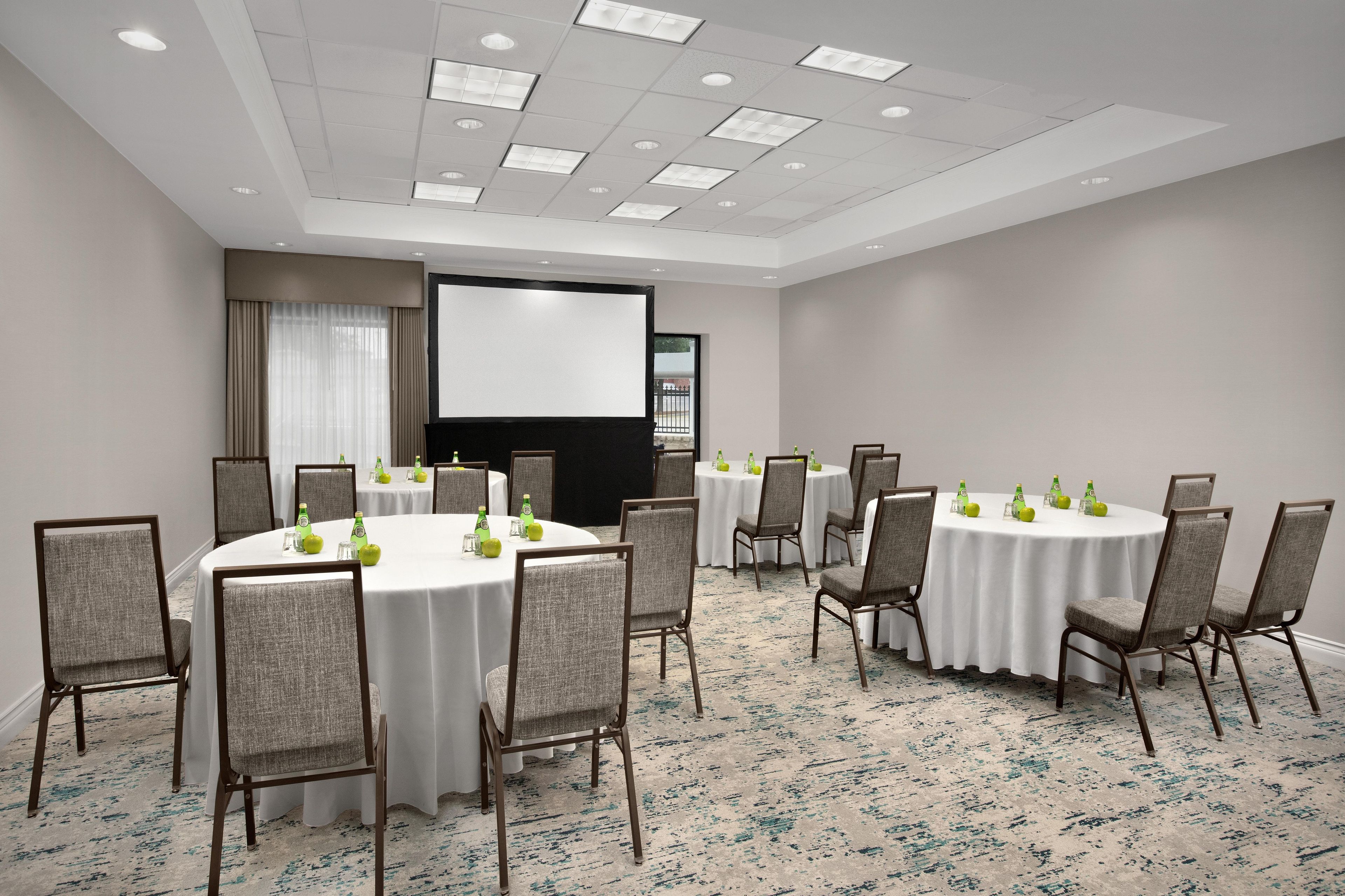 A conference room with round tables, chairs, and a projector screen.