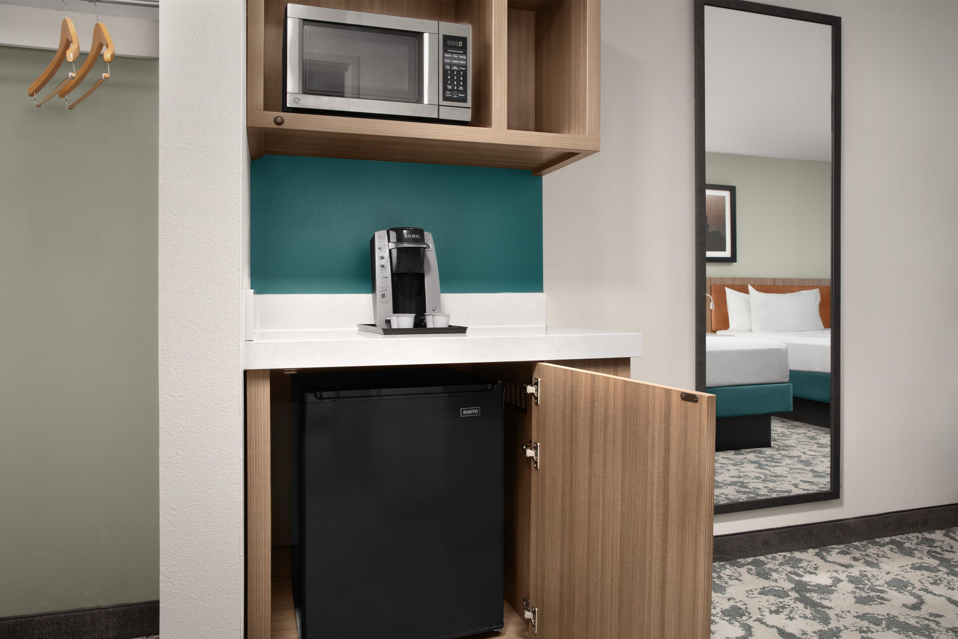 Una kitchenette compacta equipada con microondas, cafetera y un refrigerador pequeño.